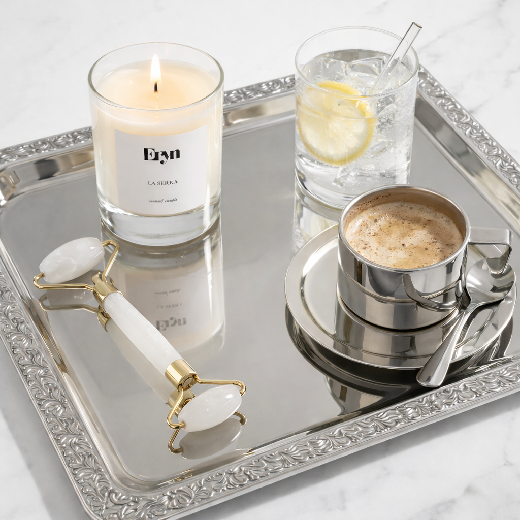 Luxury clean-burning candle by Eryn in the scent LA SERRA, a glass with lemon slice, cup of coffee, and roller on a decorative tray.